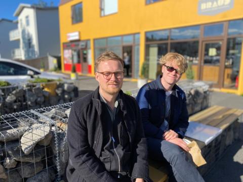 Two men sit on a bench outside Brauð &amp; Co at Laugalækur.
