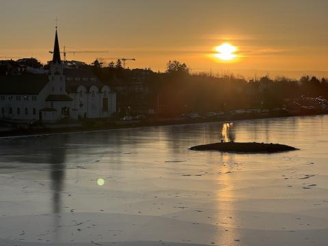 Frosin tjörn með sólarupprás í baksýn, hús í kring.
