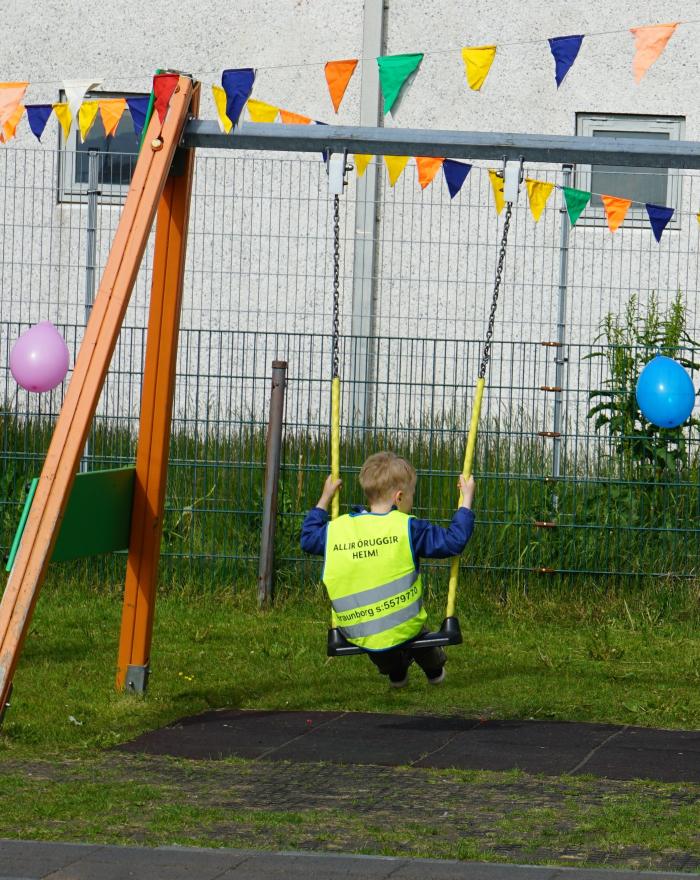 Barn að róla sér í gulu vesti á leikskólanum Hraunborg. Blöðrur og fánar í kringum róluna.