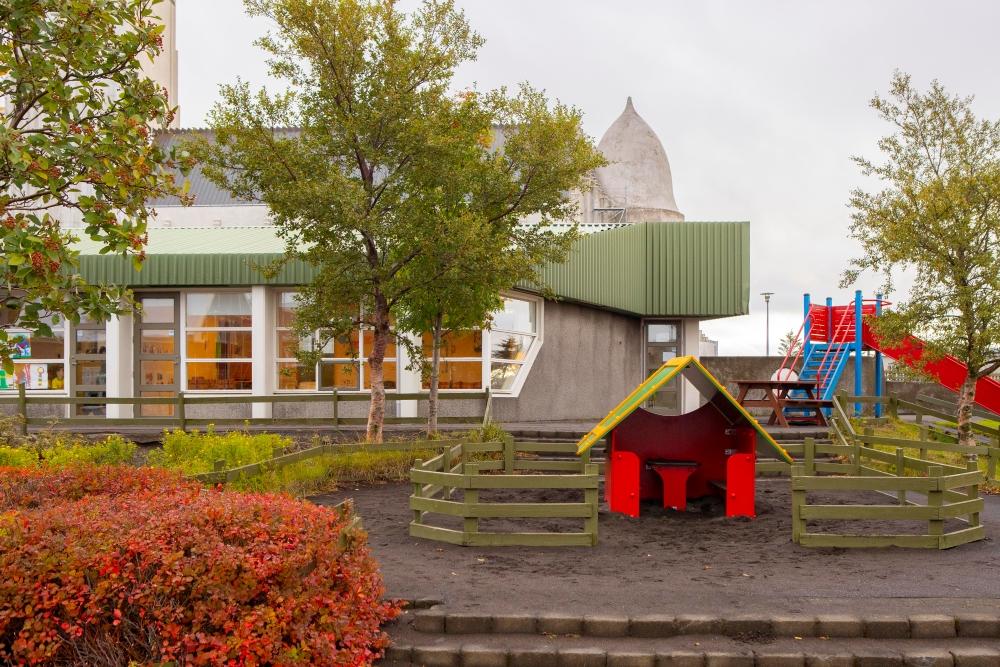 Útisvæði við leikskólann Grænuborg með litlu húsi, tré og rennibraut