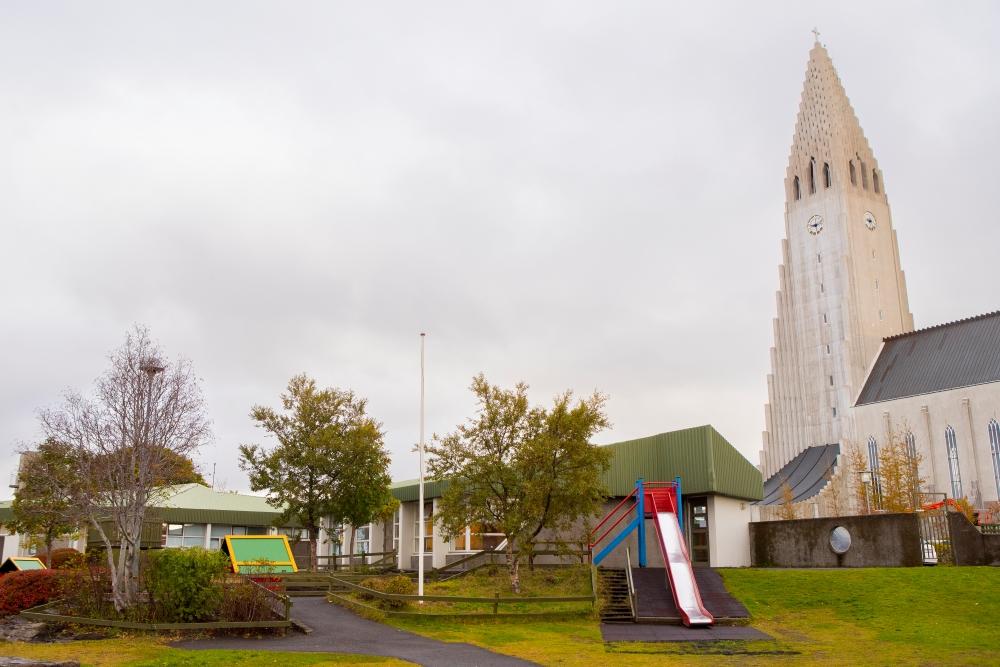 Útileiksvæði við leikskólann Grænuborg með Hallgrímskirkju í baksýn. Á leiksvæðinu má sjá rennibraut, tré og lítið hús