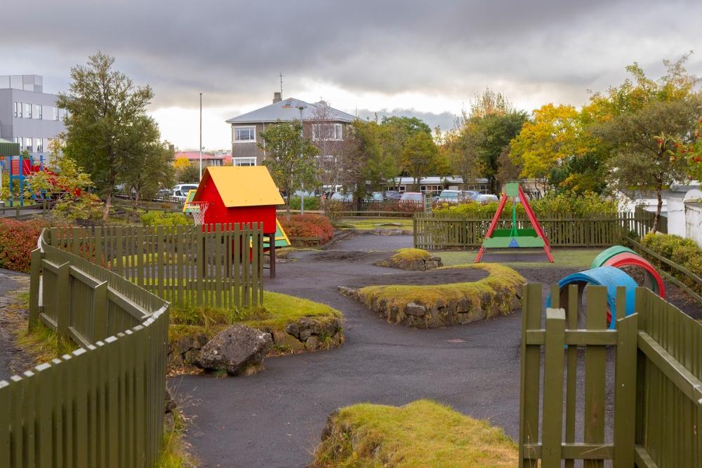 Útileiksvæði við leikskólann Grænuborg þar sem sjá má lítið hús, rólur og fleiri leiktæki.