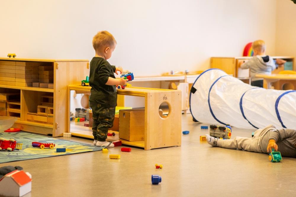 Barn að leika sér með leikfangabíl við hillur með leikfangakubbum og fleiri leikföngum á leikskólanum Björtuhlíð