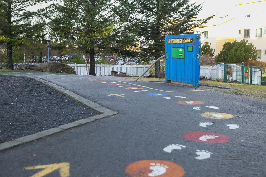 Concrete-tile surface in the outdoor area of Brekkuborg preschool. Footprints and arrows are painted on the surface, leading to a box painted like a gas station. 