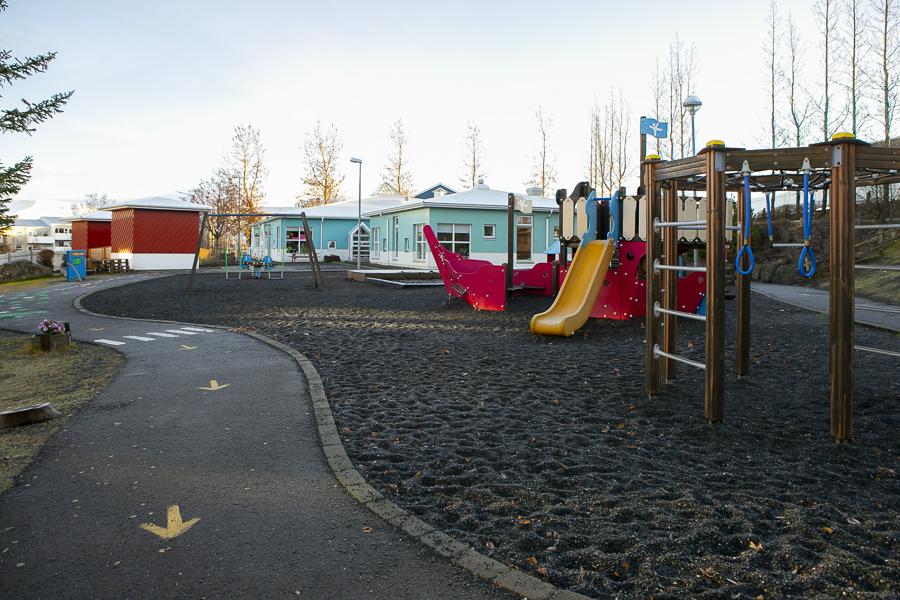 Path with arrows and walkway, outdoor playground equipment and Brekkuborg preschool building in the background