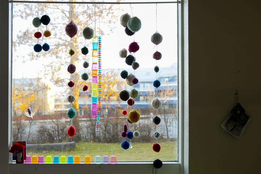 Colorful decorations made from yarn balls and plastic cups hanging in the window.