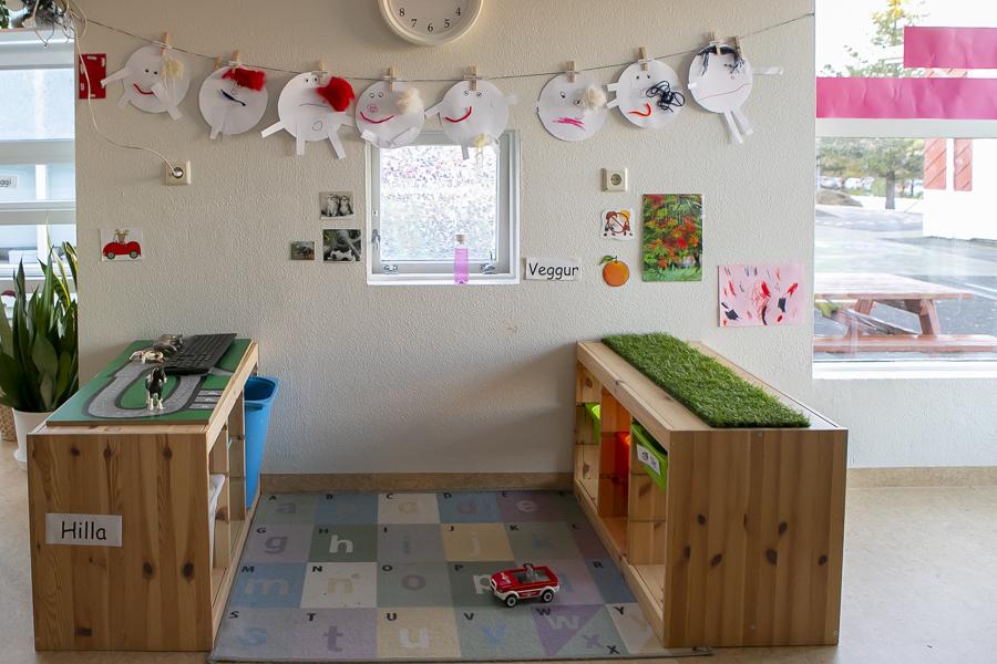 Shelves with toys, a rug, toy car and children's fine arts on the wall.