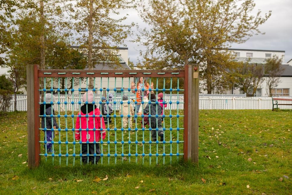 Börn í fótbolta séð í gegnum fótboltamark á útisvæði leikskólans Gullborgar