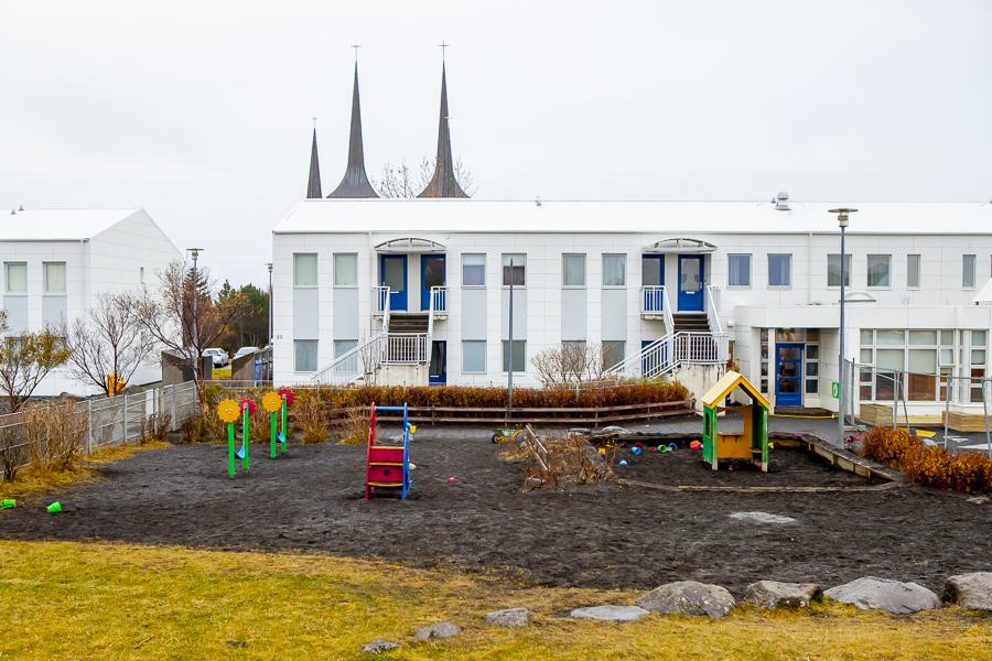Outdoor playground equipment at Klambrar. The white preschool building in the background with the towers of Háteigskirkja church.