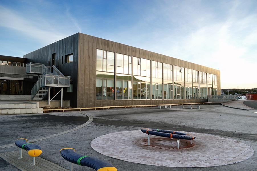 Mynd af stóru gráu húsi með gluggahlið sem hýsir Plútó félagsmiðstöð