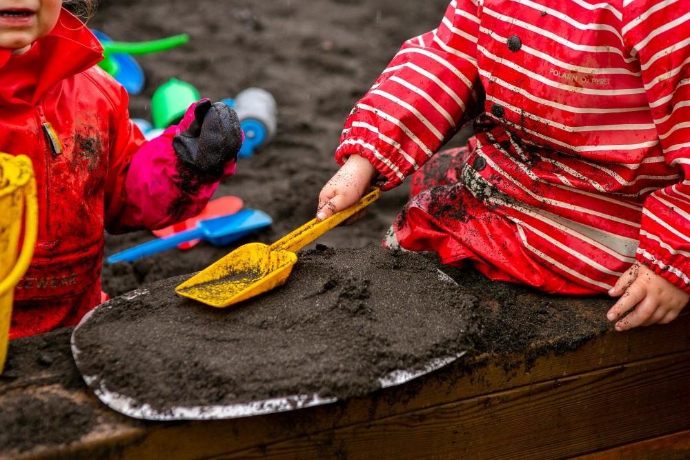 Barn að moka með skóflu í sandkassa 