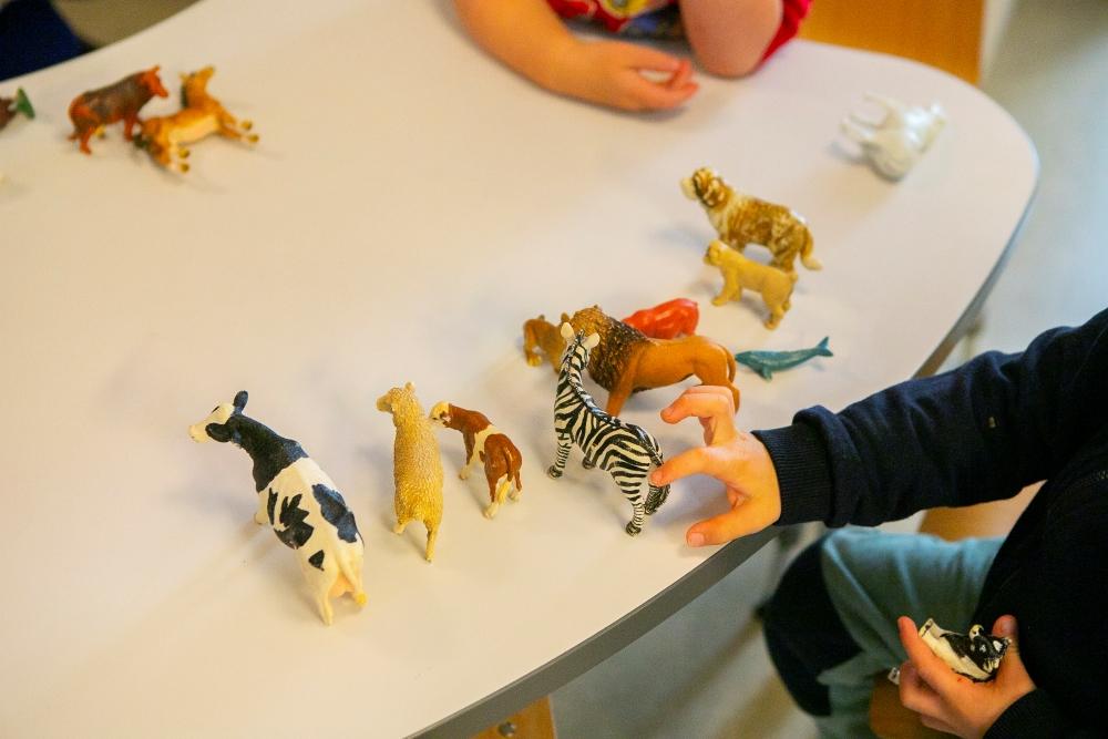 Börn að leika með plastdýr á borði