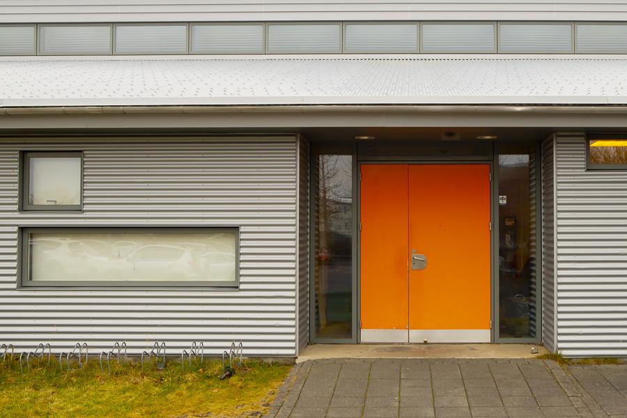 Hvítt hús með appelsínugulri hurð sem hýsir leikskólann Nes við Hamravík