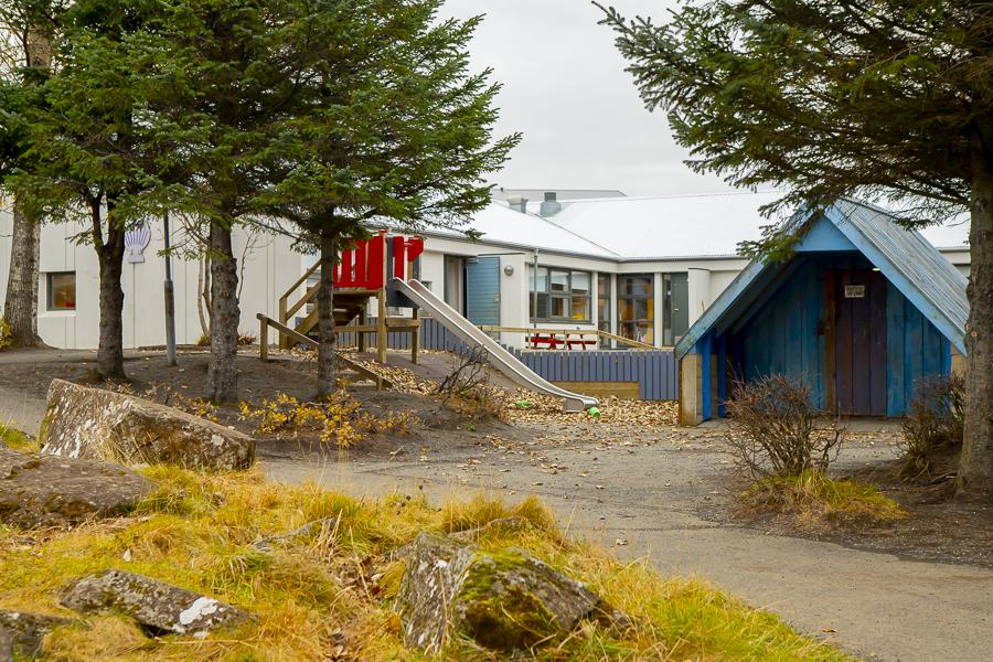 Útisvæði leikskólans Sunnufoldar með rennibraut, litlu húsi og barrtrjám