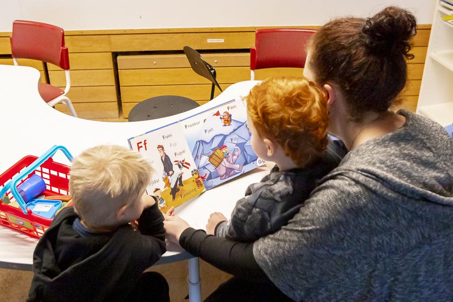Children sitting and looking at a book with a preschool teacher