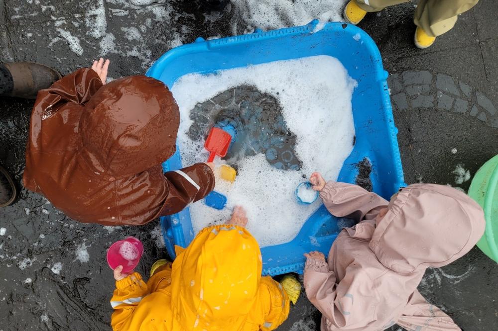 Börn í pollagöllum að sulla með vatnsbala á leikskólanum Vinagerði