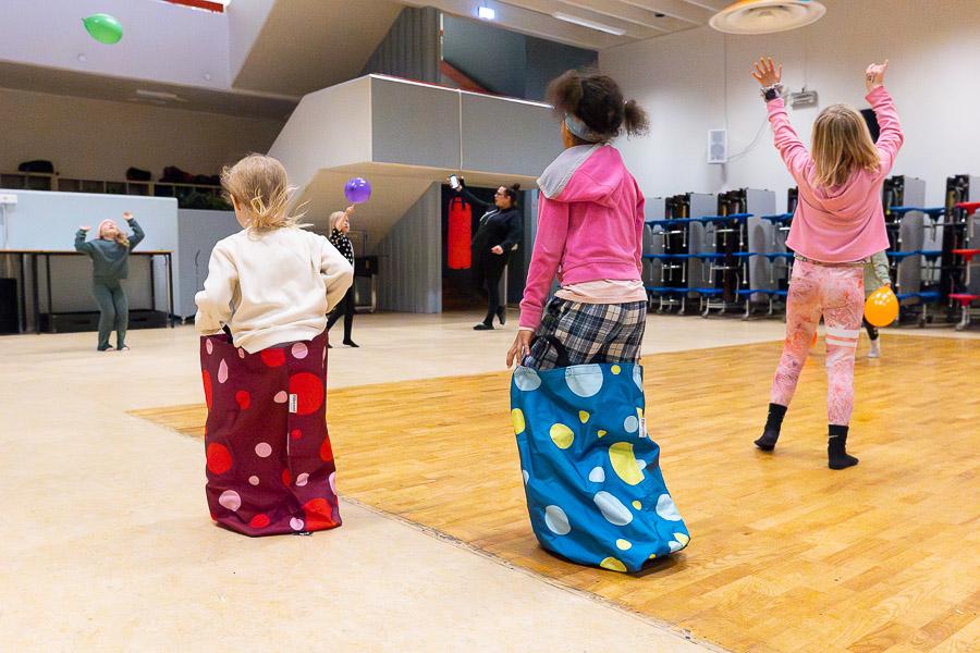 Children in sack races and playing with balloons in the gymnasium. 
