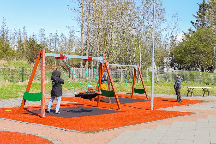 Children on swings on a red patio. 