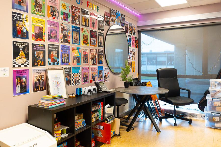 A room with a wall covered in pictures with the heading "Hall of fame." A low black shelf, a table, and chairs. A large mirror on a wall. 