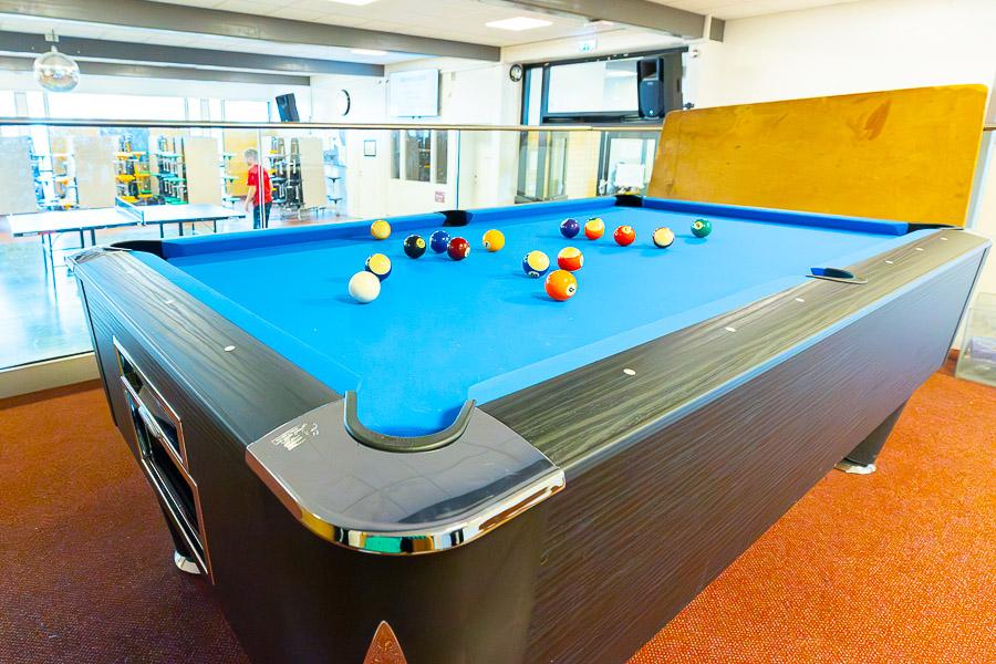 A hall with a pool table, an orange carpet, and a ping-pong table in the background. 