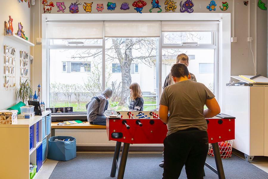 Children playing a foosball. In the background, children can be seen sitting on the windowsill. 