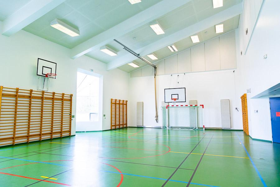 Íþróttasalur með hallandi þaki. Fótboltamark, körfuboltakarfa og klifurgrindur. 