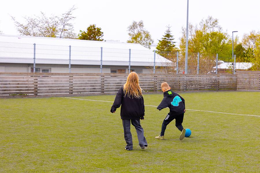 Börn að spila fótbolta á útigrasvelli.