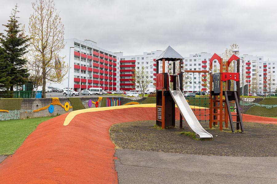 Leikvöllur með klifurkastala og rennibraut. Blokkir í baksýn.
