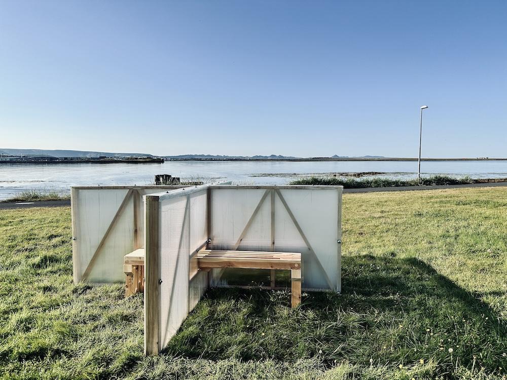 Gras, bekkir og skilrúm við sjó.