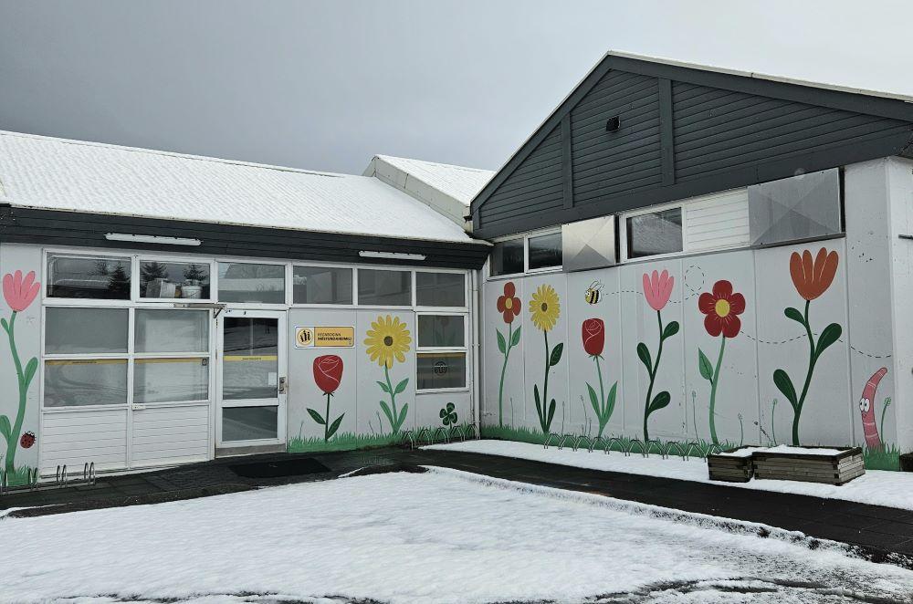 Hvítt hús með máluðum blómum á, sem hýsir frístundaheimilið Regnbogann. 