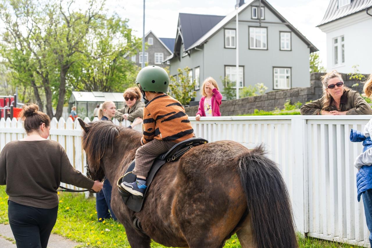 Barn á hestbaki og fullorðnir í kring.