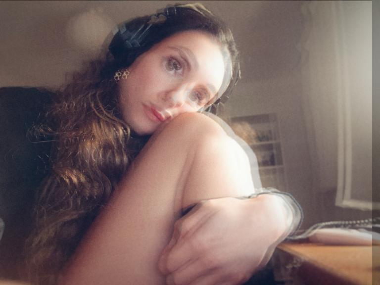 Julie Trouvé, French musician. Soft color portrait, headphones on head, sitting with knee under chin