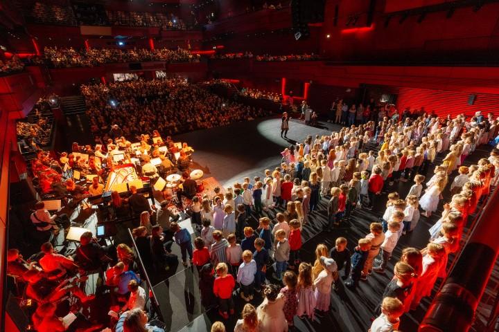 Eldborg hall with children on stage as parents, grandparents, aunts, and uncles look on.