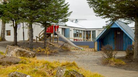 Útisvæði leikskólans Sunnufoldar með rennibraut, litlu húsi og barrtrjám