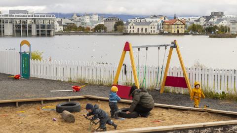 Börn í sandkassa með rólur í baksýn á útisvæði leikskólans Tjarnar