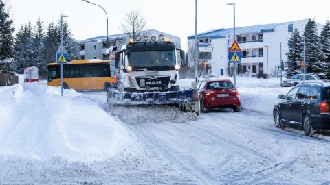 snow plow clearing a street. Snow, houses, and cars nearby.